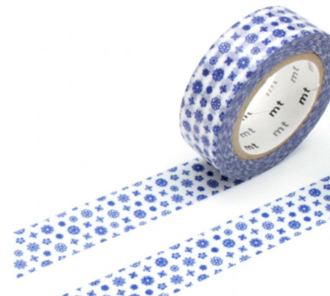A roll of washi tape with a blue snowflake and star pattern on a white background, shown with the tape unrolled out on a white surface. The inner core shows the brand name 'mt'.