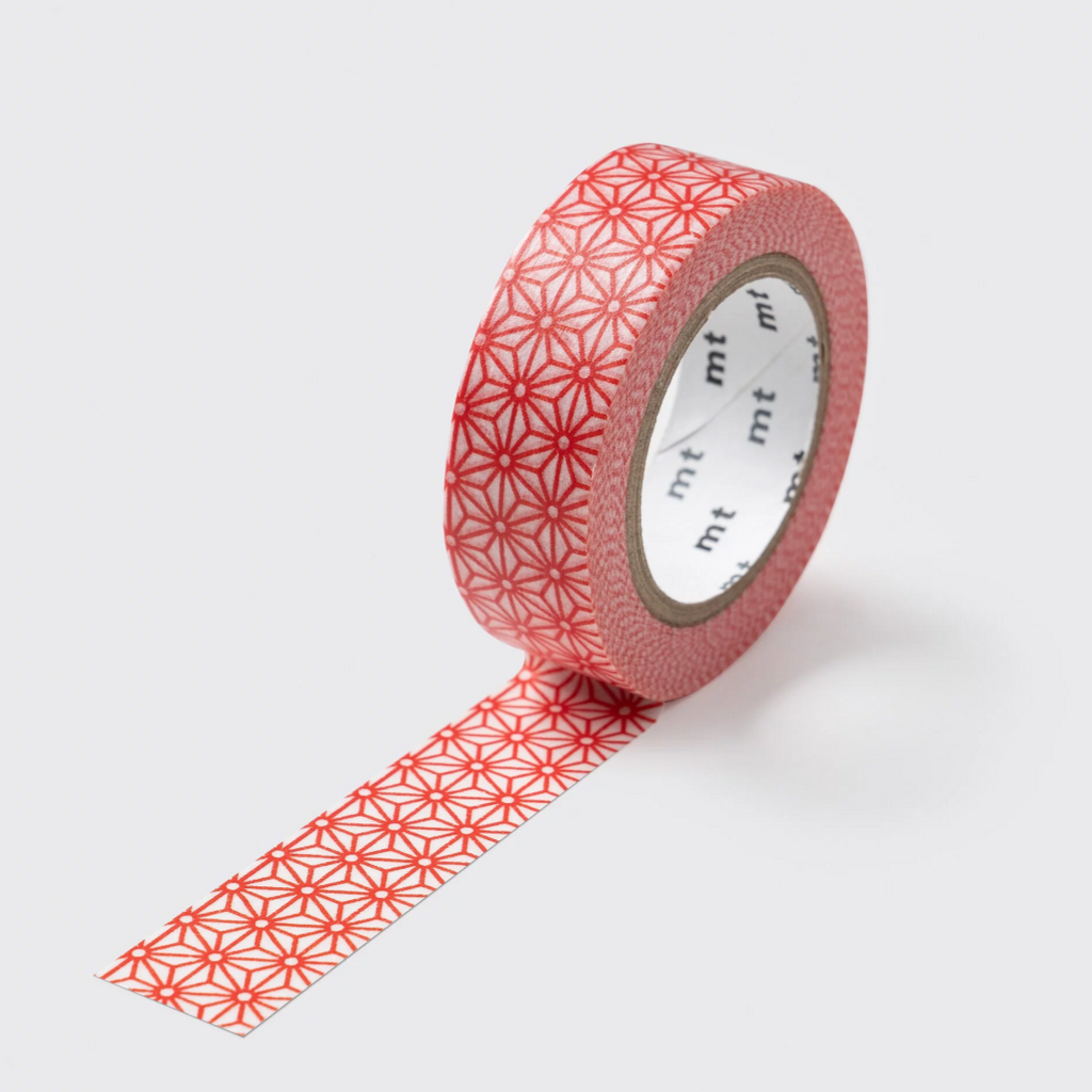 A roll of decorative washi tape with a repeating red geometric starburst pattern on a light pink background, shown with one strip unrolled against a light gray background.