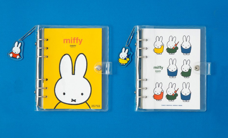Two clear plastic binder sleeves on a bright blue background. The left sleeve contains a yellow Miffy notebook with a large white bunny face and the word 'miffy' in orange.