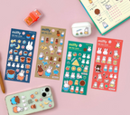 Four colorful Miffy-themed sticker sheets arranged on a pink background, along with a decorated phone case, a white earbud case, a small orange stamp, and part of a planner. The sheets feature cartoon bunnies and cute illustrations in blue, beige, green, and red.