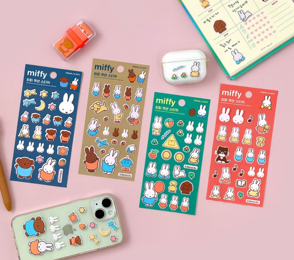 Four colorful Miffy-themed sticker sheets arranged on a pink background, along with a decorated phone case, a white earbud case, a small orange stamp, and part of a planner. The sheets feature cartoon bunnies and cute illustrations in blue, beige, green, and red.