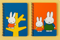 Miffy! Two spiral-bound notebooks with colorful cartoon rabbit covers, displayed side by side on a yellow background. The left notebook has a blue cover with a white rabbit on a yellow tree, and the right notebook has an orange background with two white rabbits in orange and green outfits.