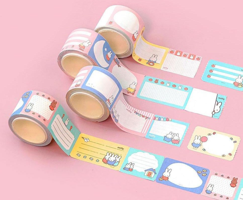 A set of pastel washi tapes and matching label sheets with cute cartoon bunny illustrations, arranged on a solid pink background. Miffy